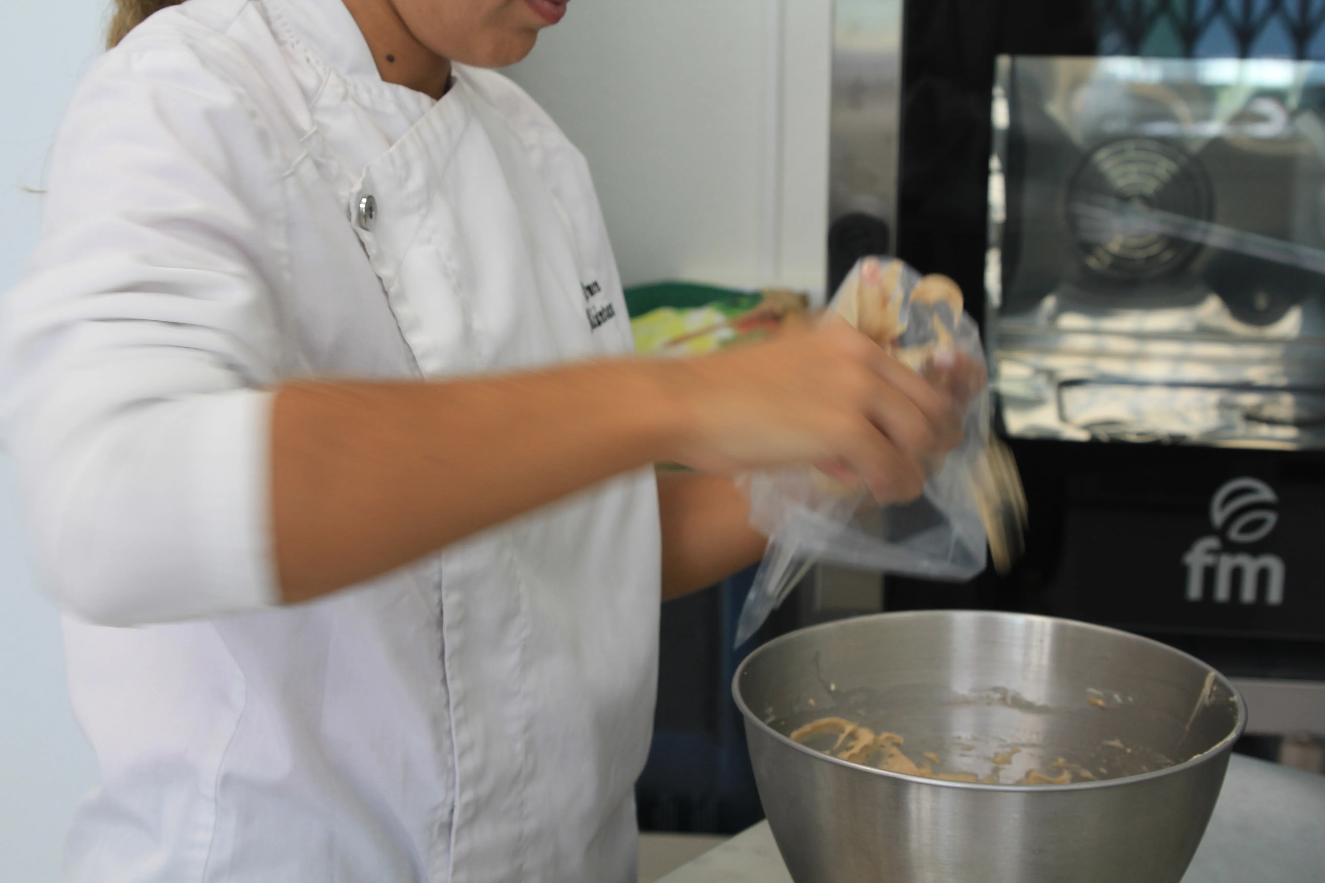 Llenando una manga pastelera sobre un bol de acero, junto al horno del obrador.
