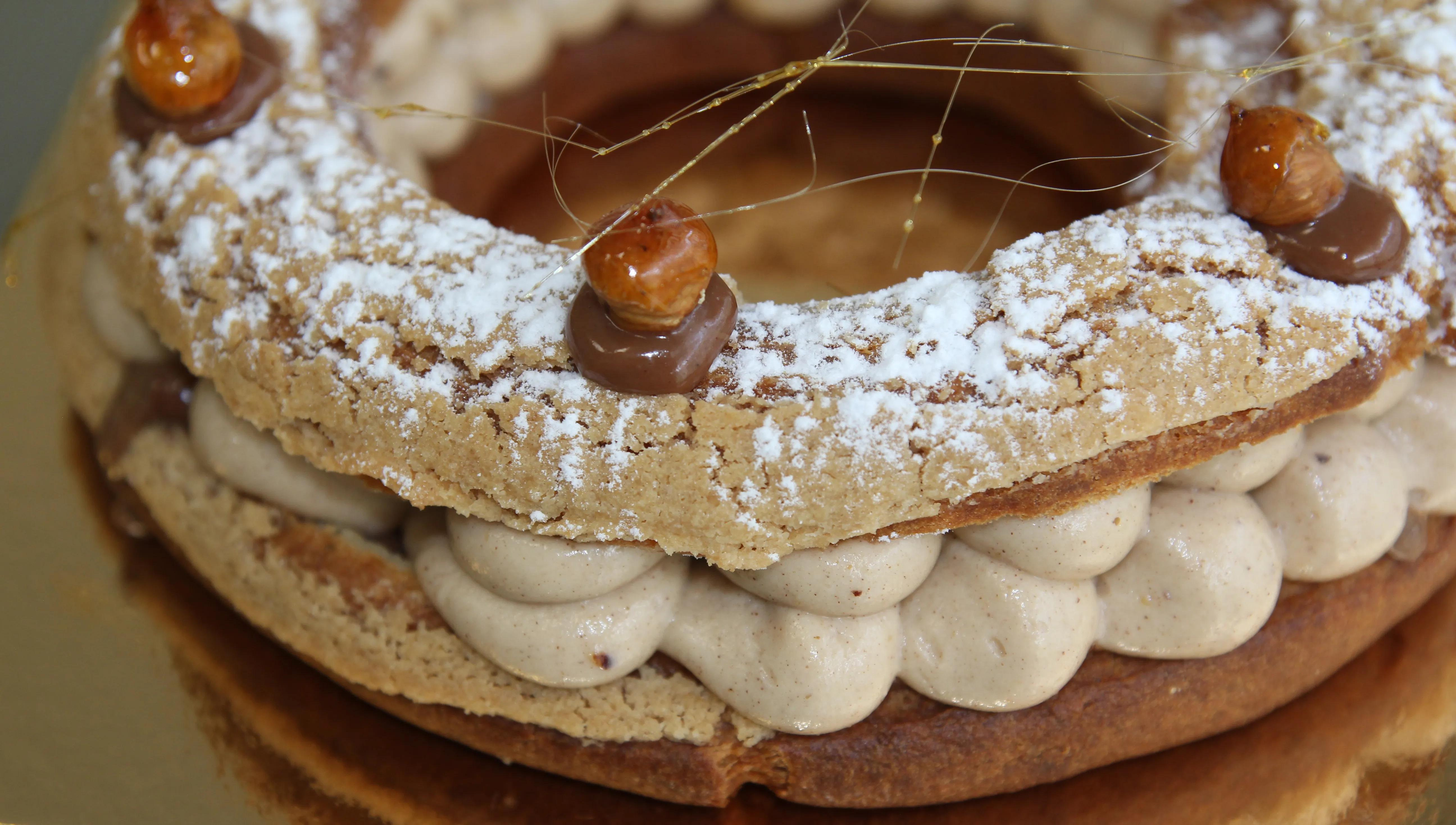 París-Brest de cerca: corona de choux con azúcar glas, crema de avellana a manga y avellanas caramelizadas con hilos de caramelo.