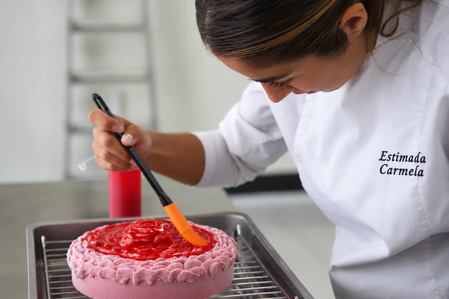 Pintando a pincel el glaseado rojo de una tarta rosa con borde de merengue, sobre la rejilla del obrador.