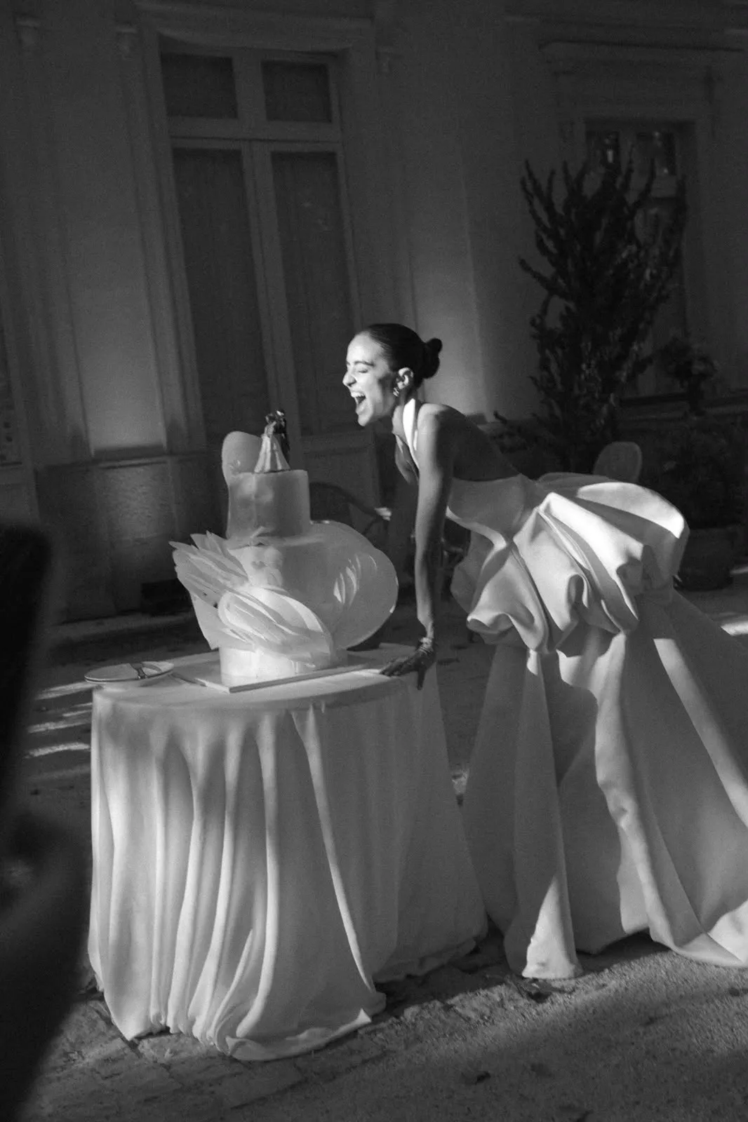 La novia junto a la tarta de volantes blancos, en blanco y negro.