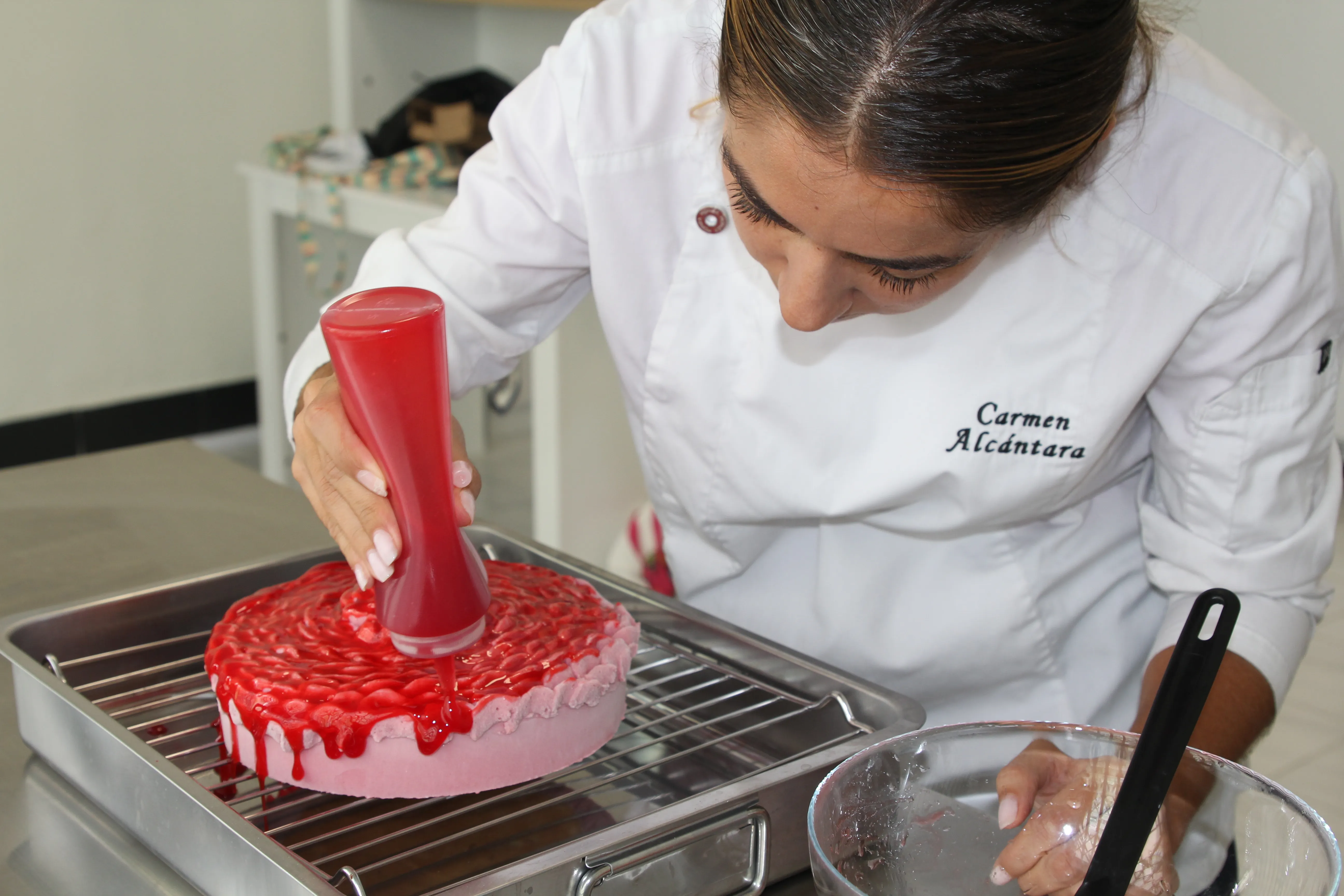 Glaseado rojo vertido con un biberón sobre la tarta rosa, en una rejilla del obrador.