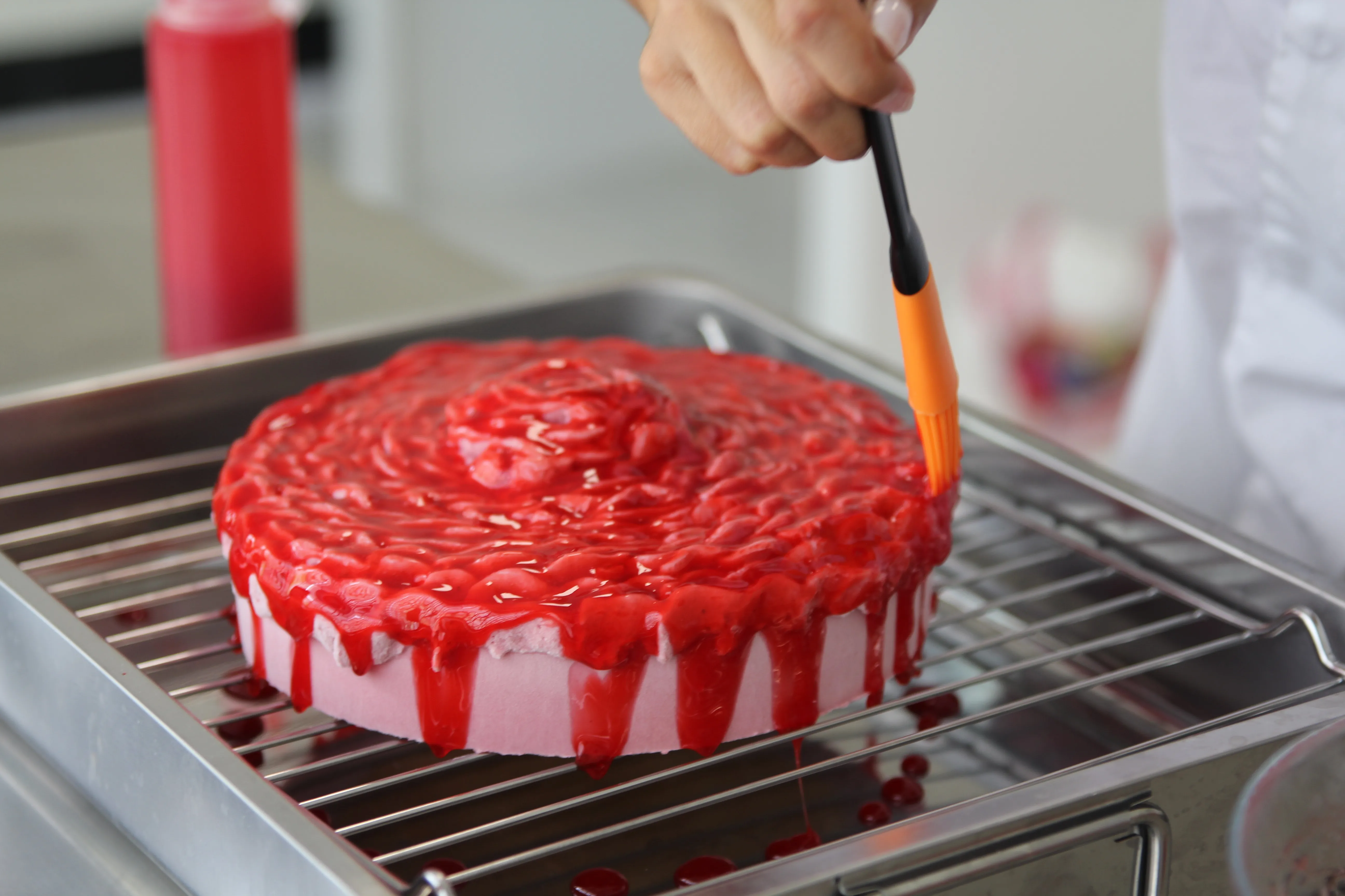 El glaseado rojo de la tarta rosa se extiende a pincel y cae por los bordes.