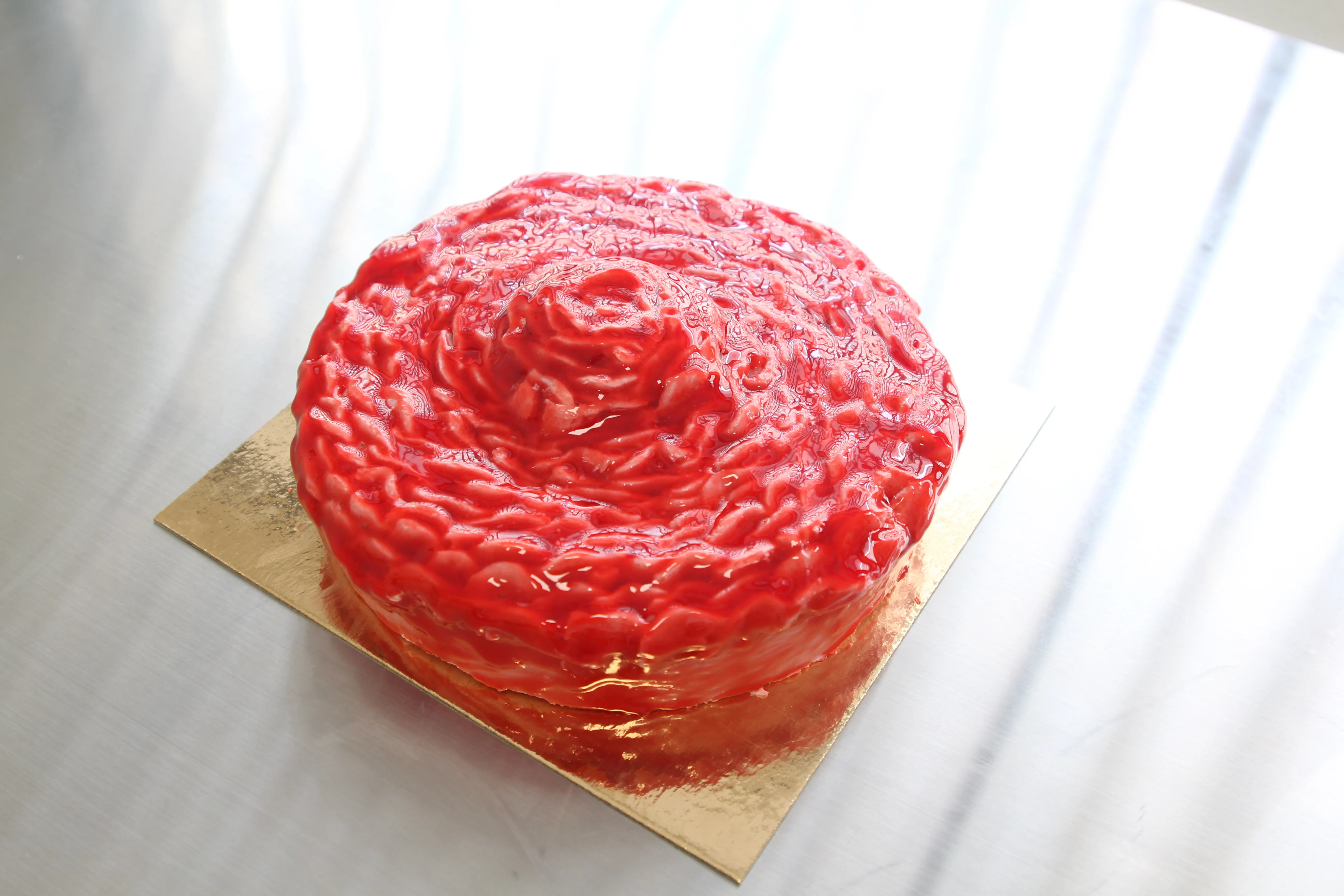 La tarta terminada, de glaseado rojo en espiral, sobre una base dorada.
