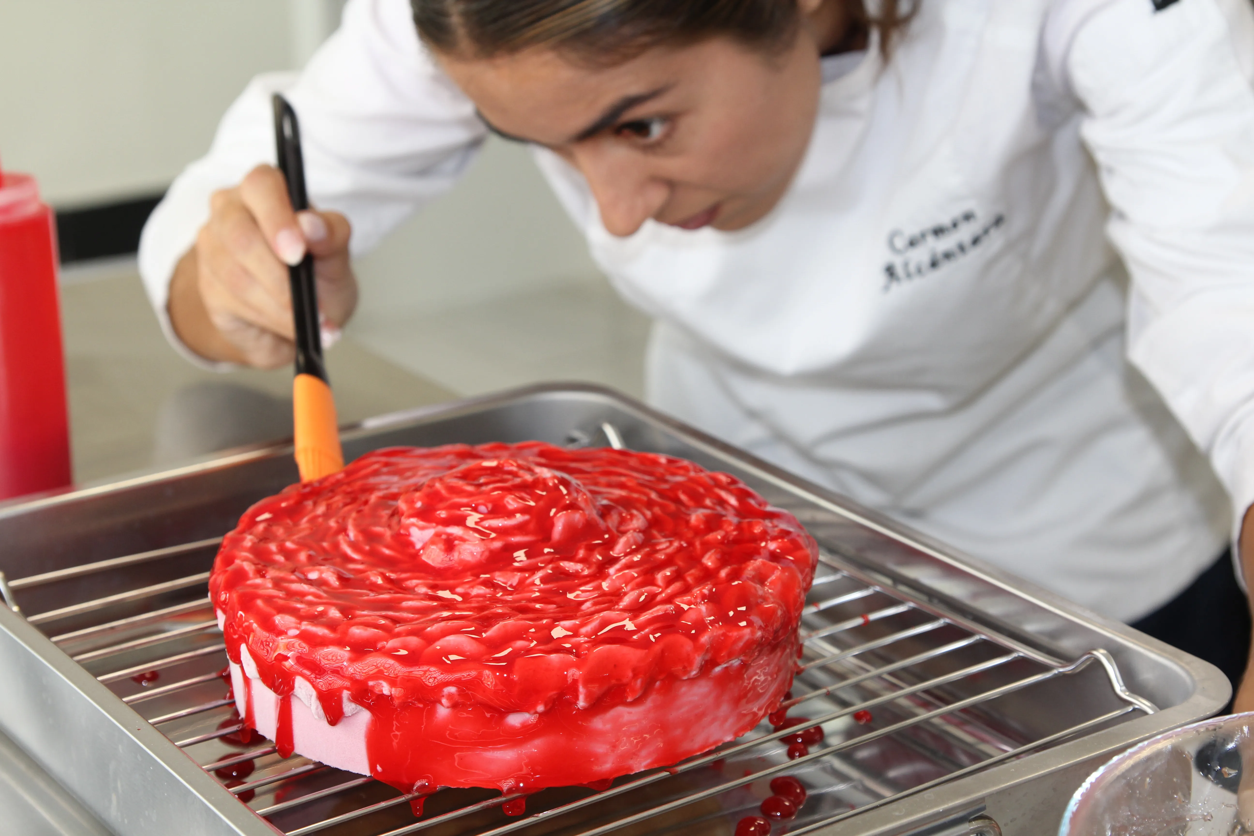 Pintando a pincel el glaseado rojo de una tarta sobre la rejilla del obrador, muy de cerca.